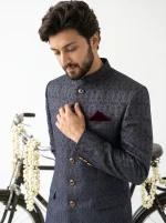 Men’s luxury charcoal grey Jacquard prince coat with intricate textured patterns, golden buttons, and maroon pocket square, paired with a premium silk shalwar kameez for weddings and formal occasions.