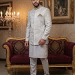 Luxury silver Prince Coat for men with embellished collar and textured design, paired with white shalwar kameez for weddings and groom wear.